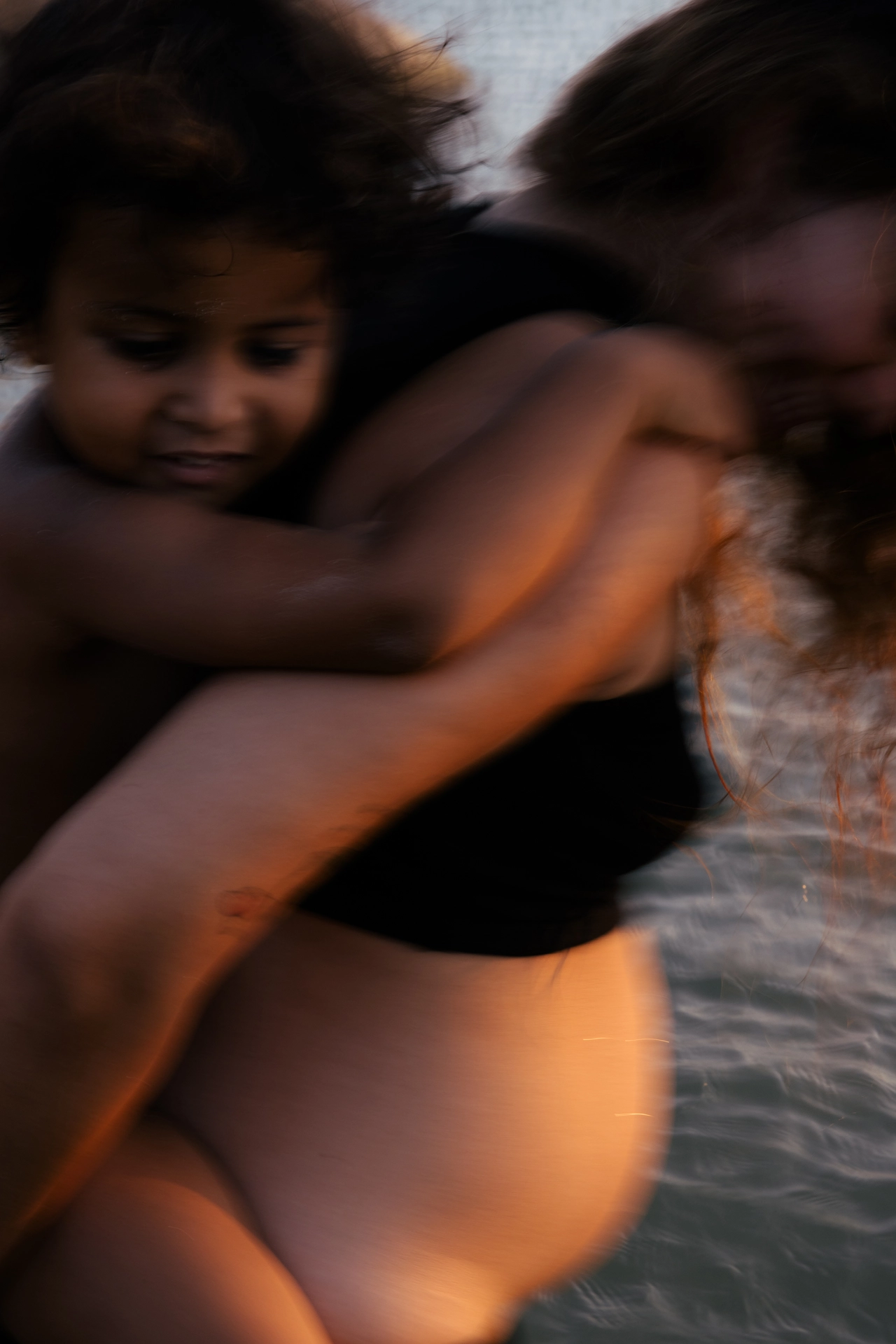 Two people embracing in water with warm, golden light illuminating their skin in a tender moment together