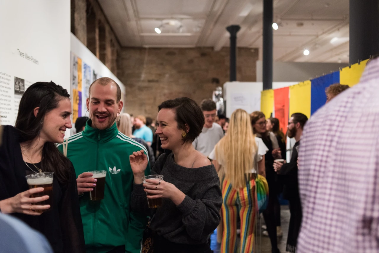 Attendees at an indoor event chat and enjoy drinks, with colourful bunting visible in the background and display panels on the walls