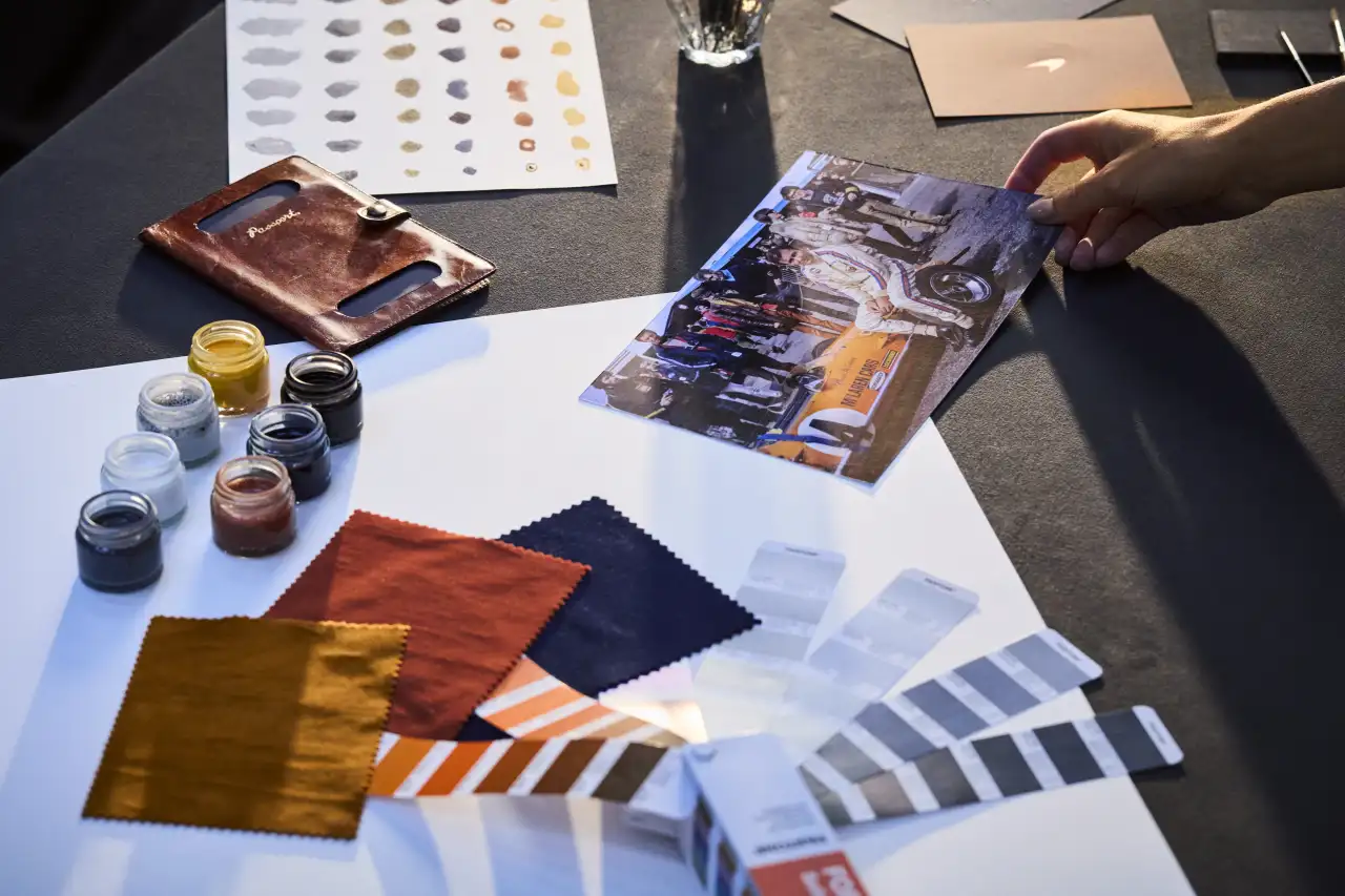 Designer's workspace showing fabric swatches in orange, navy and gold, paint colour samples, leather material, and packaging samples for McLaren's brand identity refresh