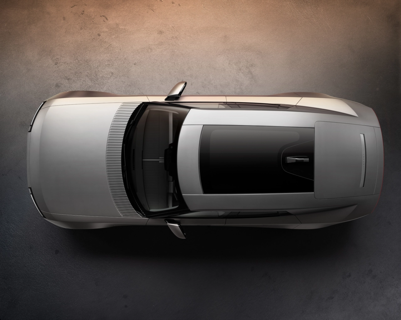 Overhead view of a silver Jaguar Type 01 with the driver's door open, showing the vehicle's boxy silhouette against a textured grey background