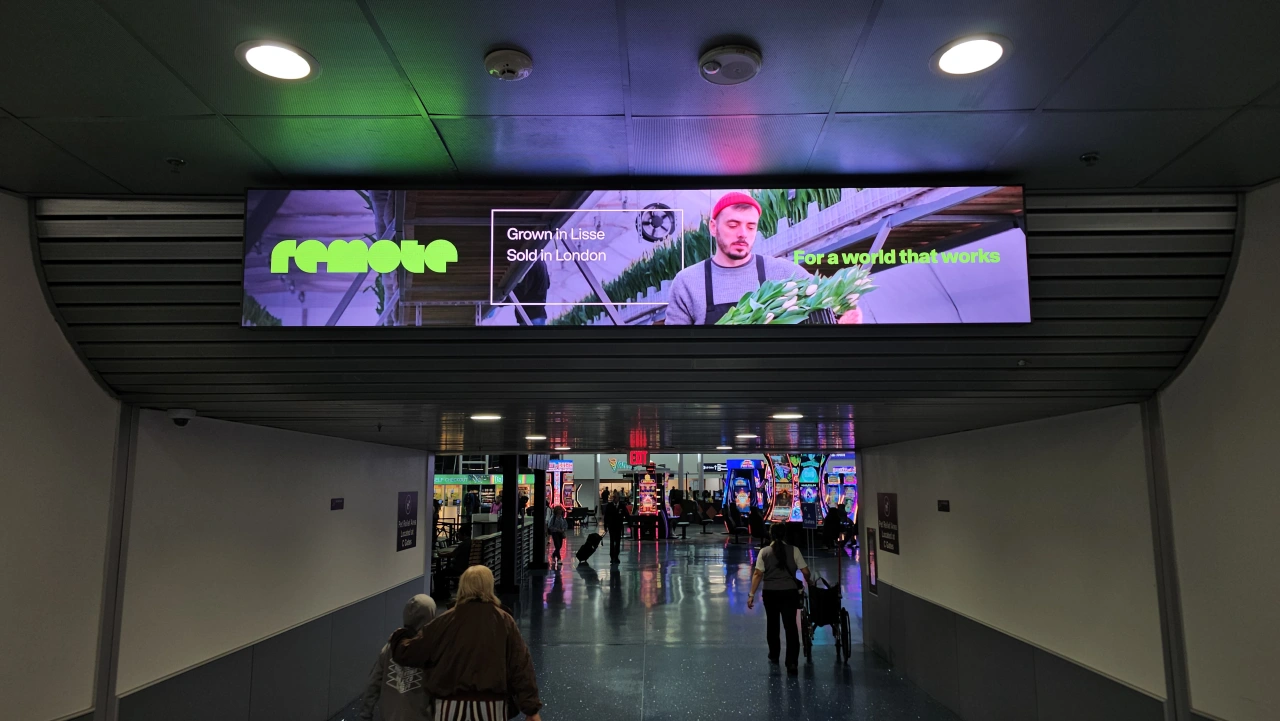 Purple and green illuminated digital screens displaying Remote branding in an airport or transit terminal walkway with pedestrians below