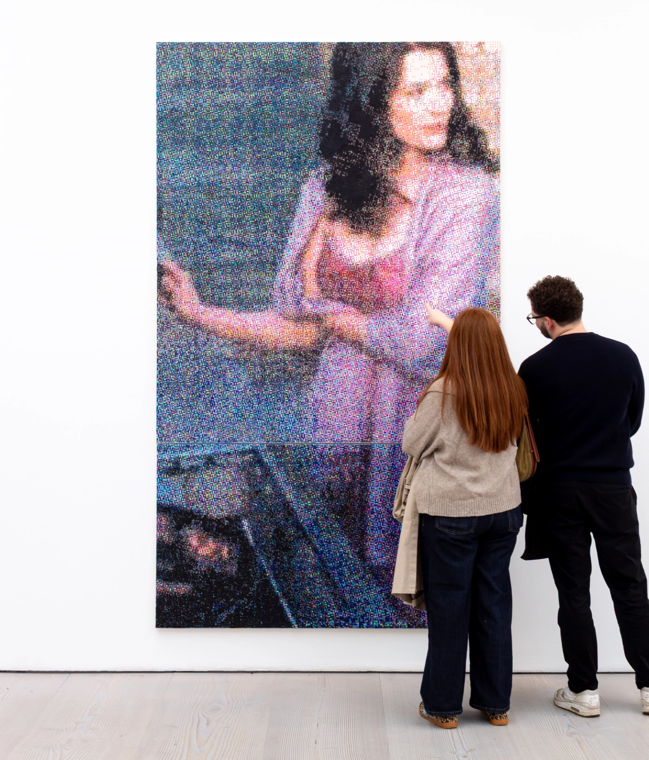 Two gallery visitors view a large pixelated painting of a woman in purple tones by Lily Bunney at the Saatchi Gallery