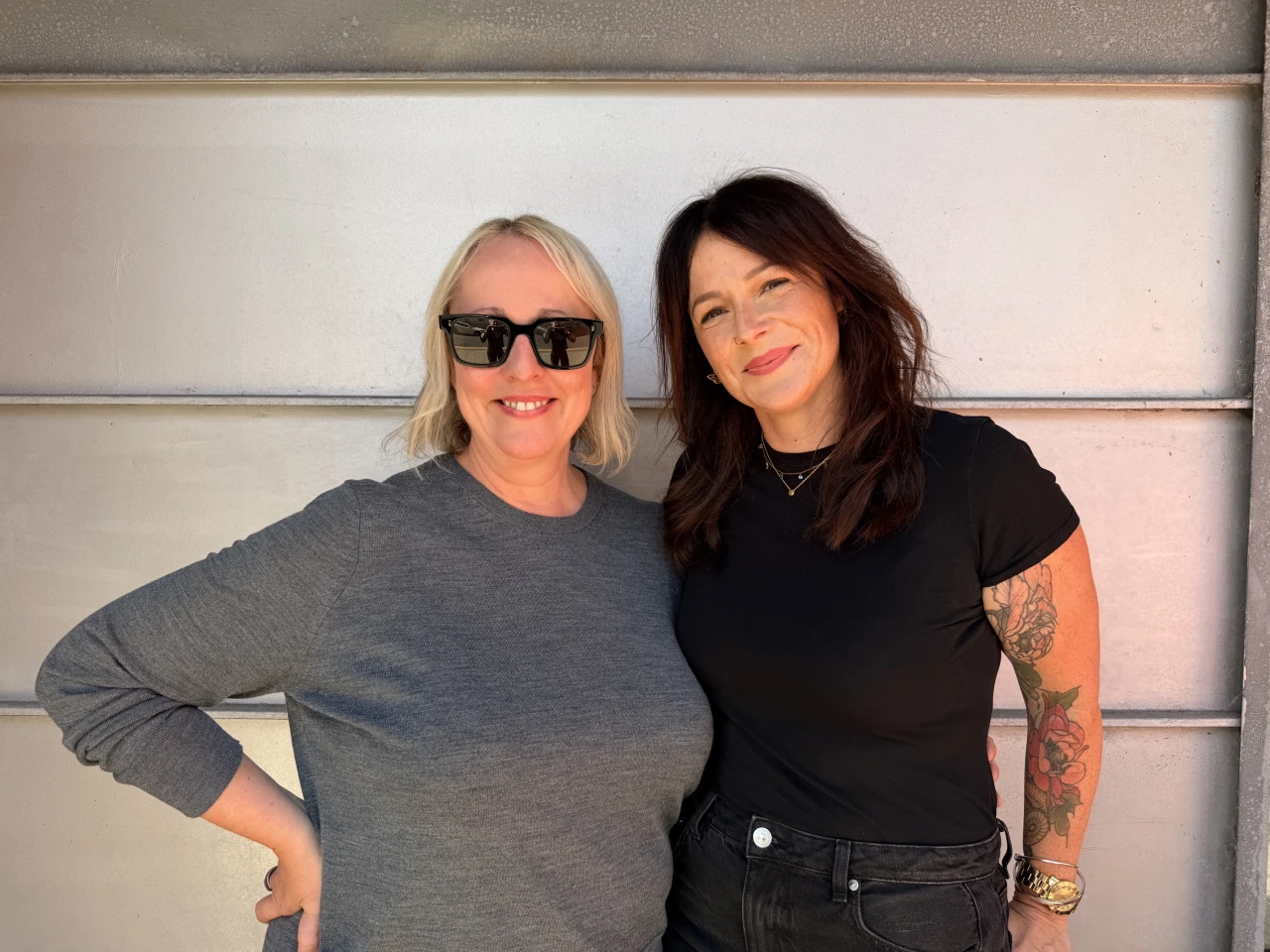 Claire Blyth and Cher Keane pose together in front of a white panelled wall