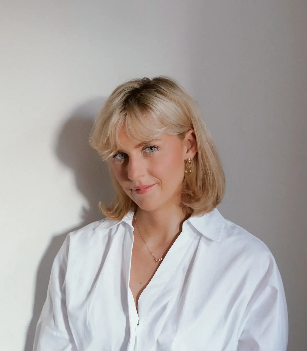 Professional headshot of a woman with shoulder-length blonde hair wearing a white shirt against a neutral background