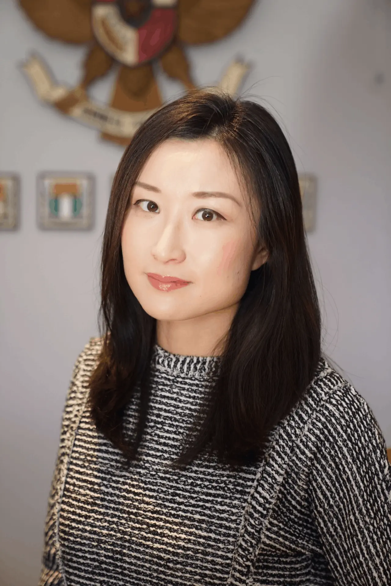 Elspeth Cheung, head shot wearing a striped knit jumper against a neutral background with branded signage visible behind her