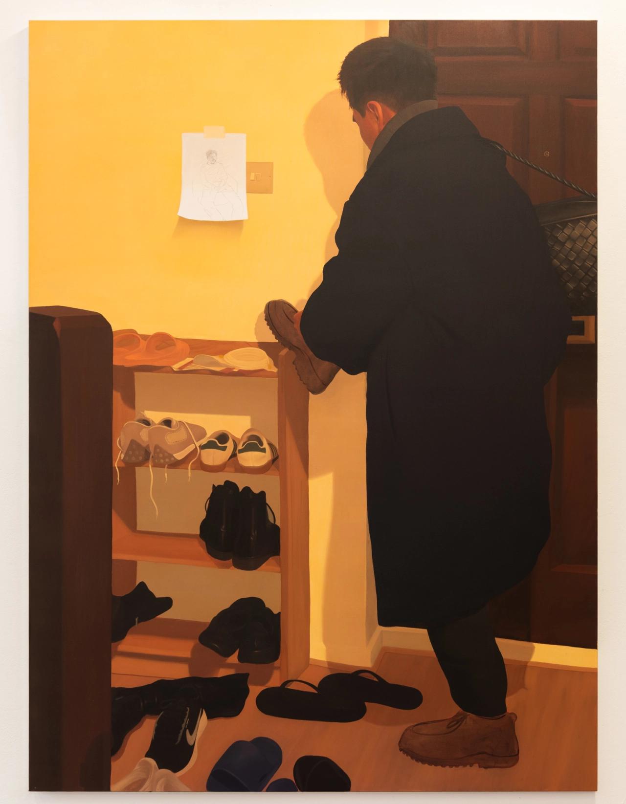 Person in black coat selecting shoes from a wooden rack in a warm-toned interior space