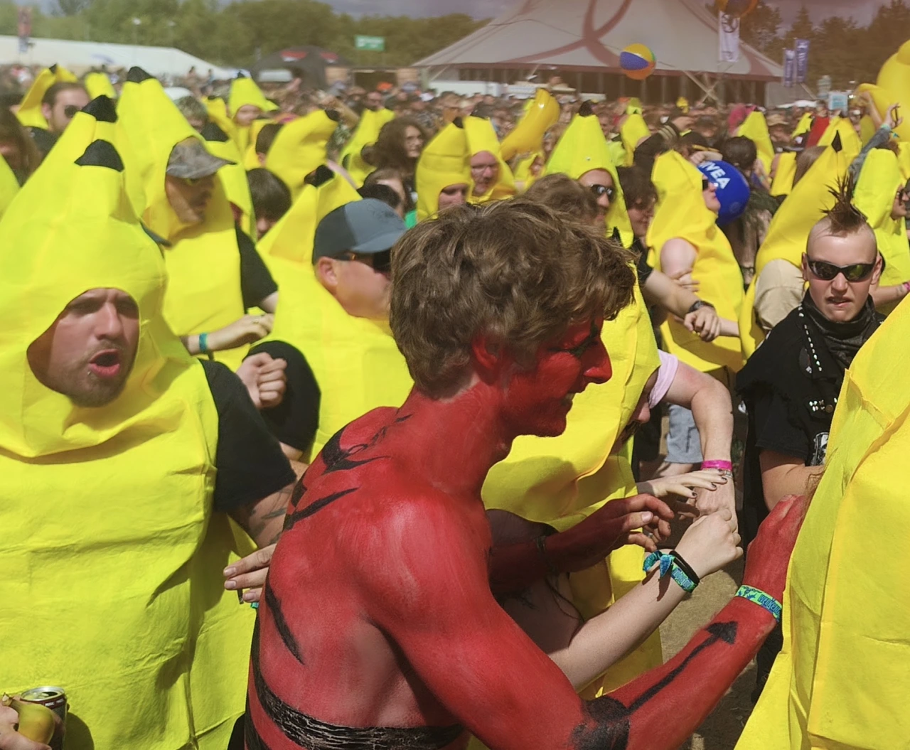 Shirtless performer with red body paint surrounded by crowd members wearing bright yellow costumes at a festival