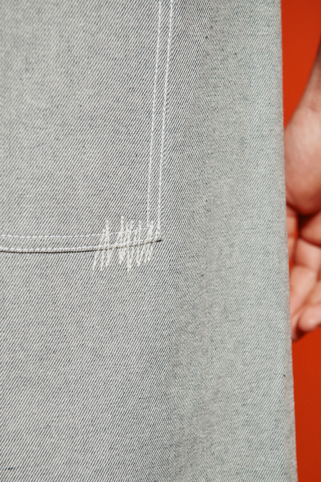 Close-up of grey fabric with vertical stitching seam and a hand holding red fabric edge against white ribbed textile
