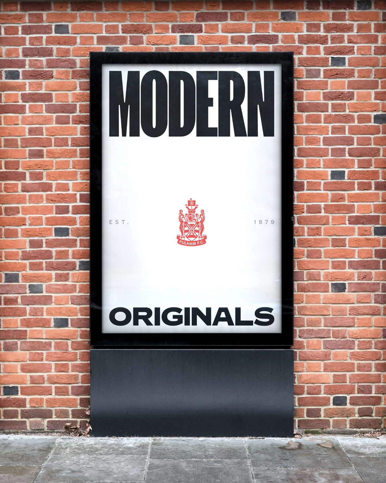 Black framed sign mounted on red brick wall reading "MODERN" at top and "ORIGINALS" at bottom with a red heraldic crest in the centre and dates either side