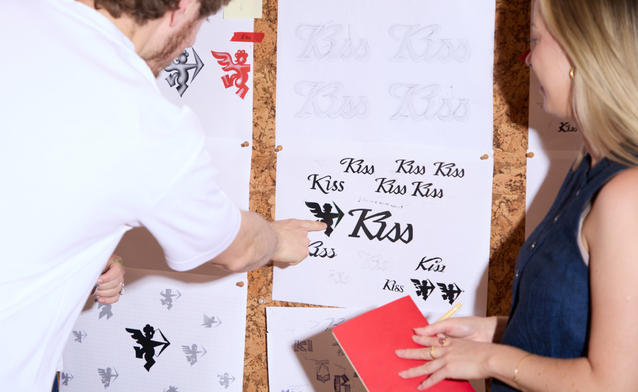 Two people examine printed materials with "Kiss" text and designs displayed on cork boards during Kiss Branding's rebrand process