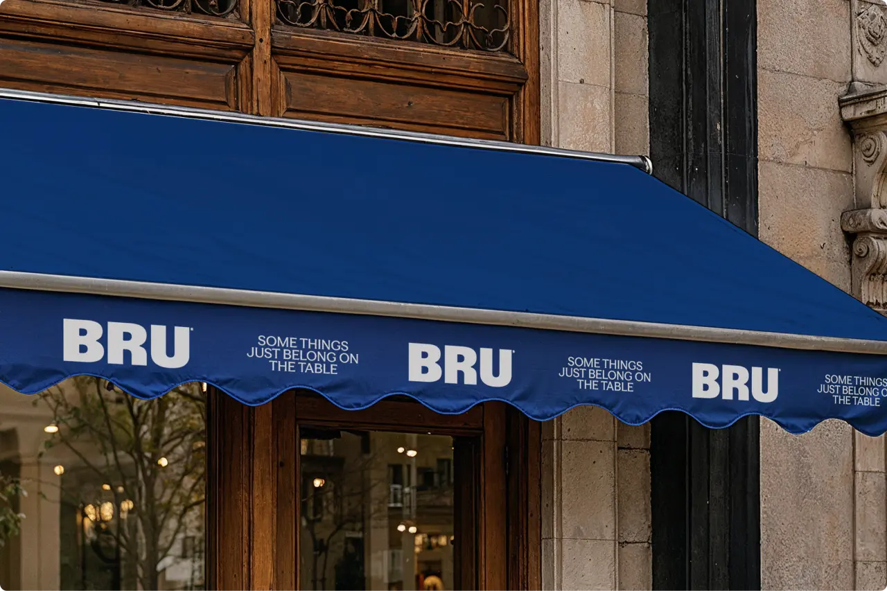 Blue awning above a restaurant entrance featuring BRU branding and "Some things just belong on the table" tagline, with elegant wooden doors and stone facade behind