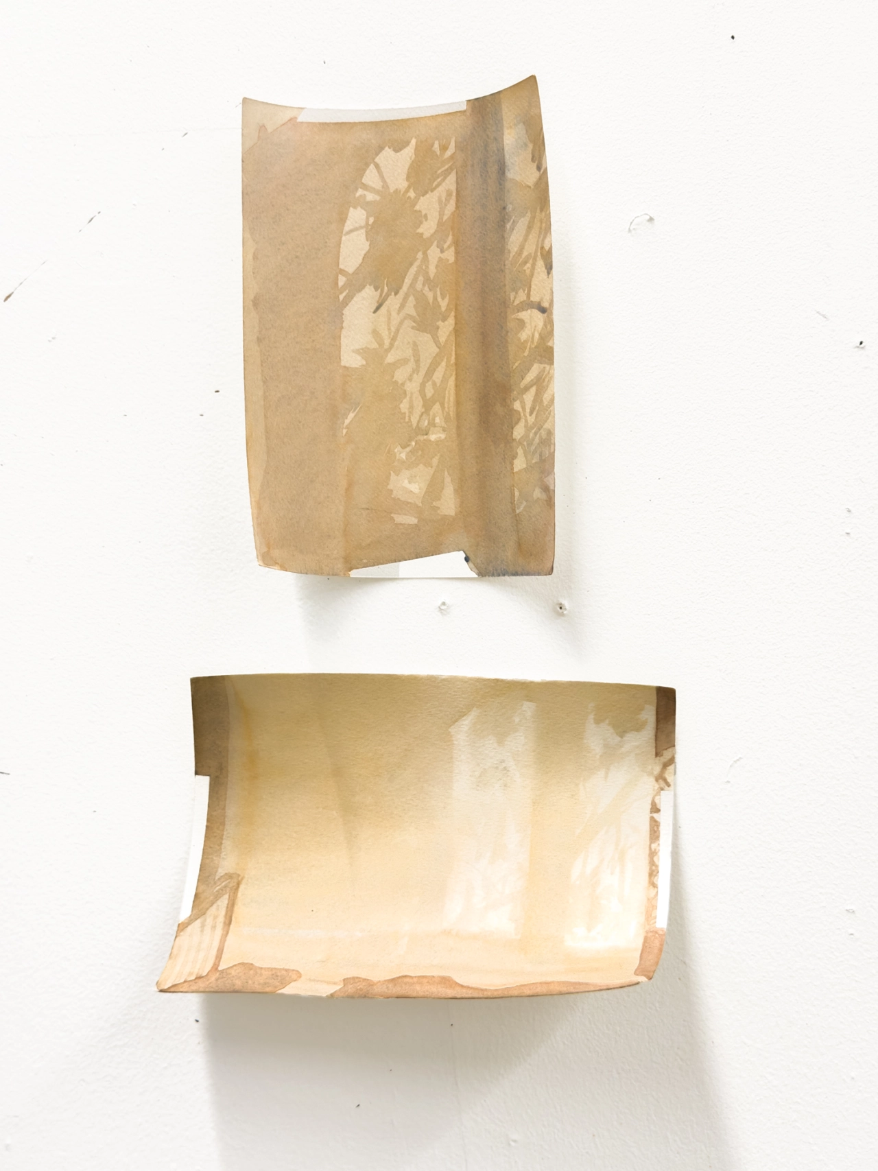 Two translucent brown paper bags mounted on a white wall, one folded vertically and one horizontally, casting soft shadows