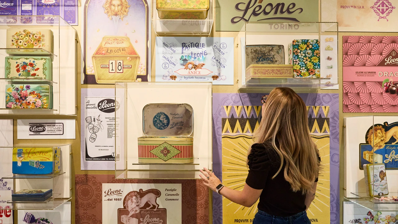 Woman examining colourful vintage sweet packaging and ephemera displayed on a wall at Leone's Happiness Factory installation