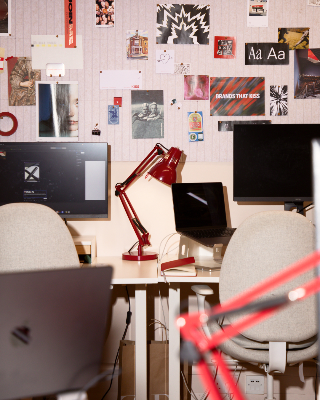 Creative studio workspace with monitors, red desk lamp, laptop and wall covered with design references and typography samples