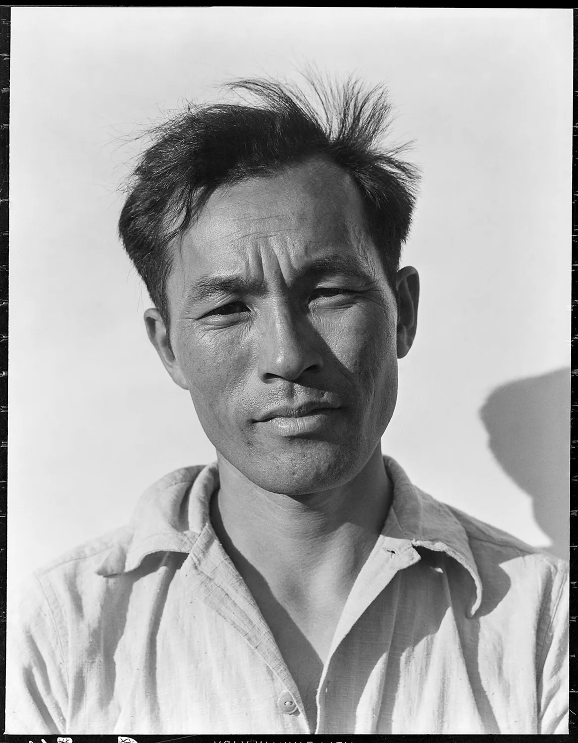 Black and white portrait photograph of a man in a light-coloured shirt at Manzanar internment camp