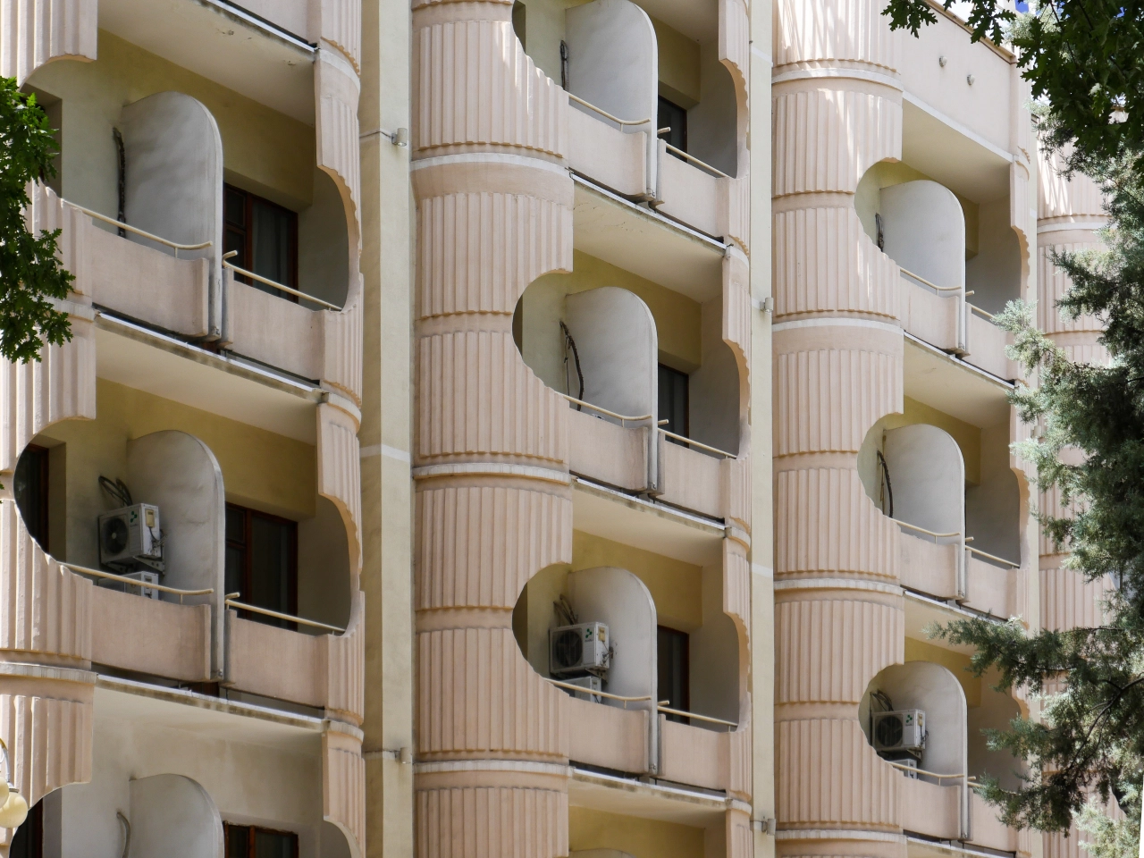 Cream-coloured brutalist apartment building with curved balconies and fluted pilasters, featuring ivy on the right side