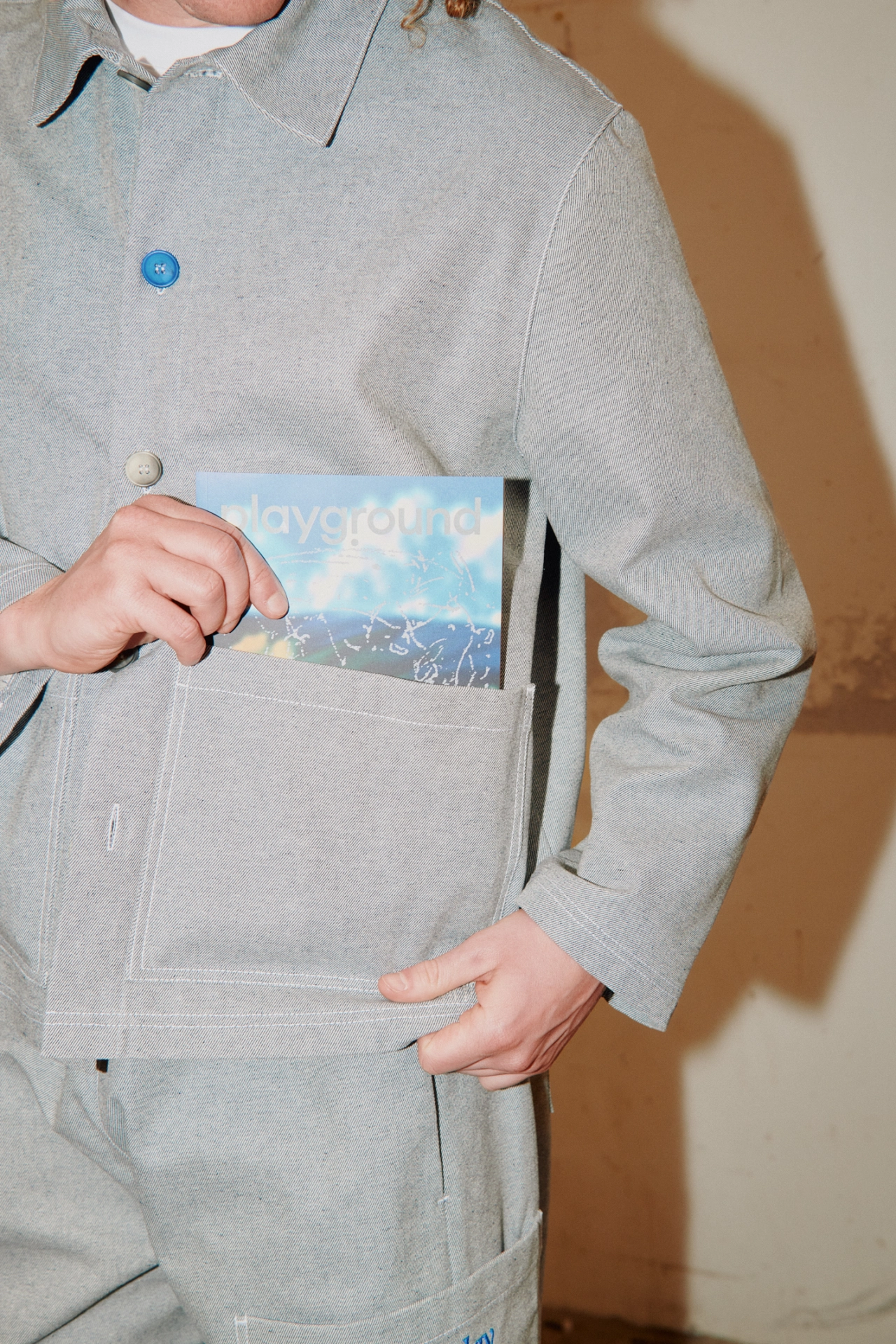 Person wearing a beige workwear jacket with blue button, holding a small blue card from the inside pocket