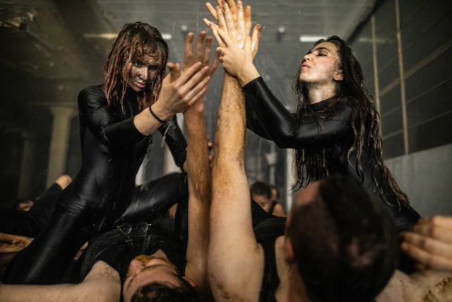 Two performers in black clothing wash a participant's raised arm under running water during the immersive Chapter Five/KAIHOGYO experience