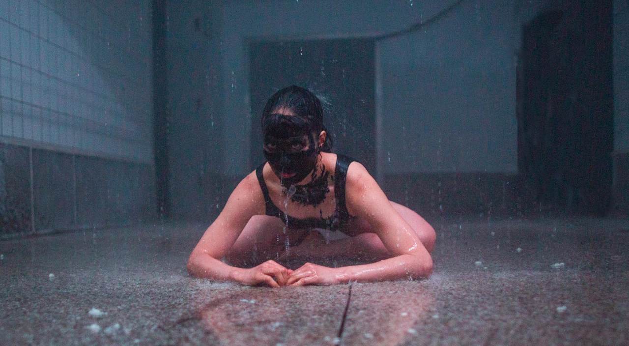Performer crouched on wet floor in tiled room during immersive art experience Chapter Five/KAIHOGYO