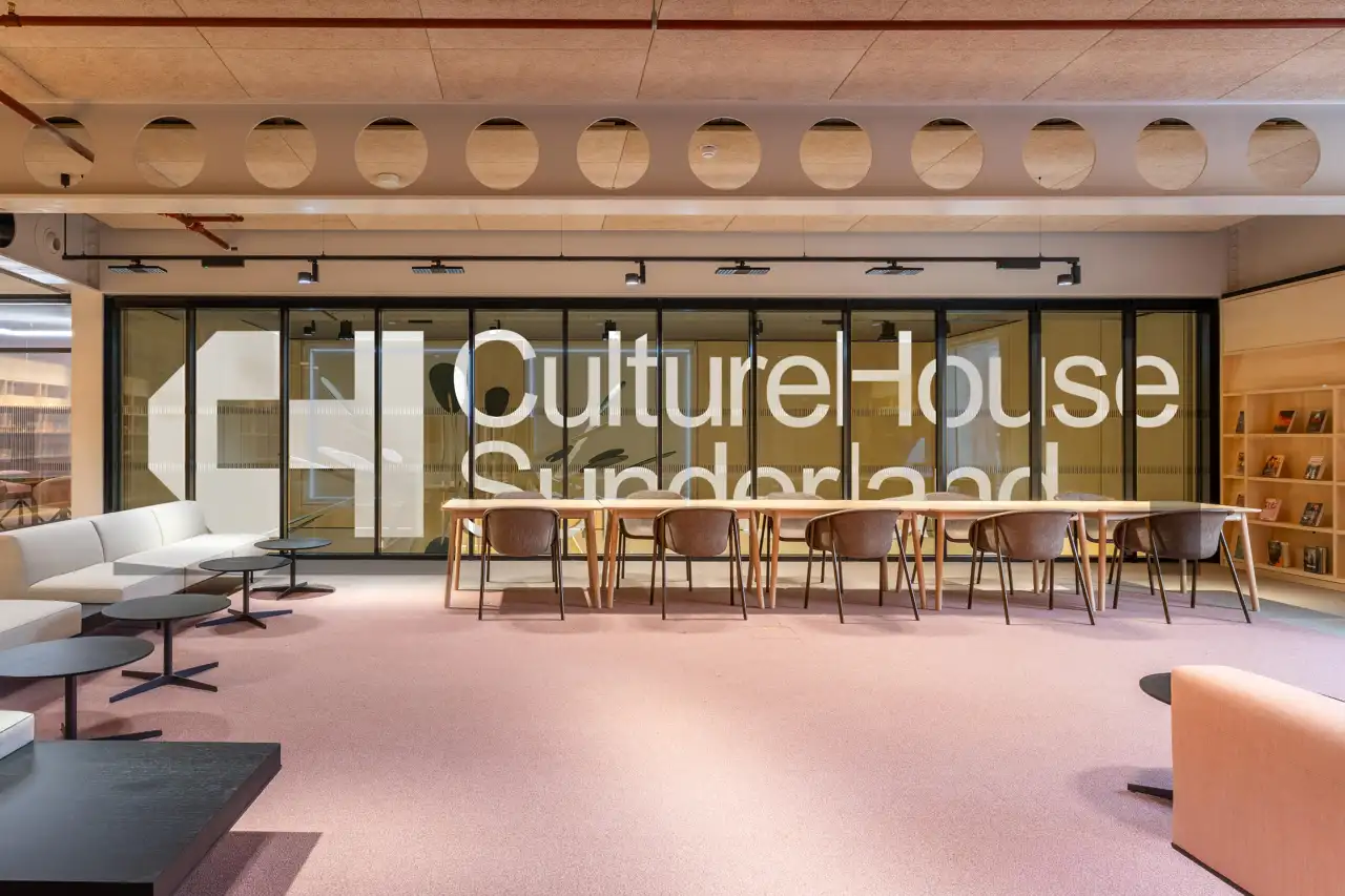 Culture House Sunderland's interior features a pink floor, dining tables with wooden chairs, and large windows with white lettering displaying the venue's name