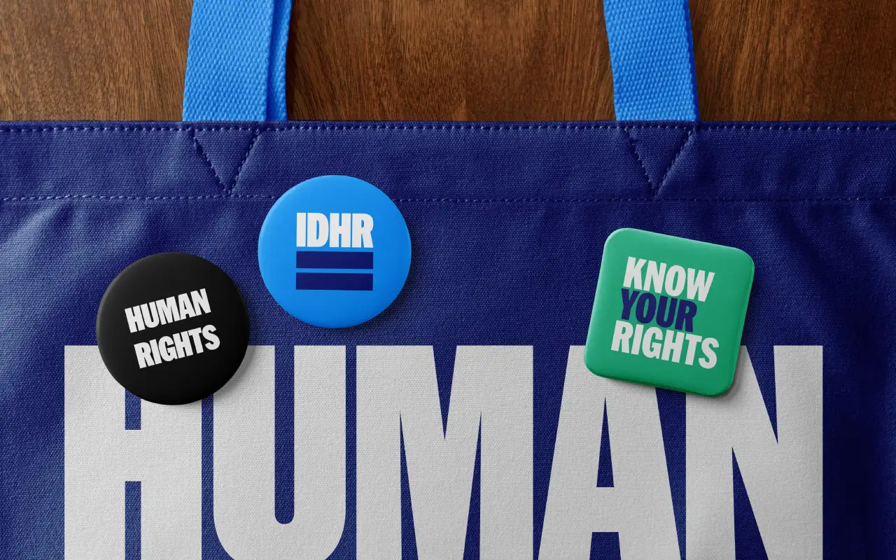 Blue tote bag with IDHR branding and three badges reading "Human Rights", "IDHR" and "Know Your Rights