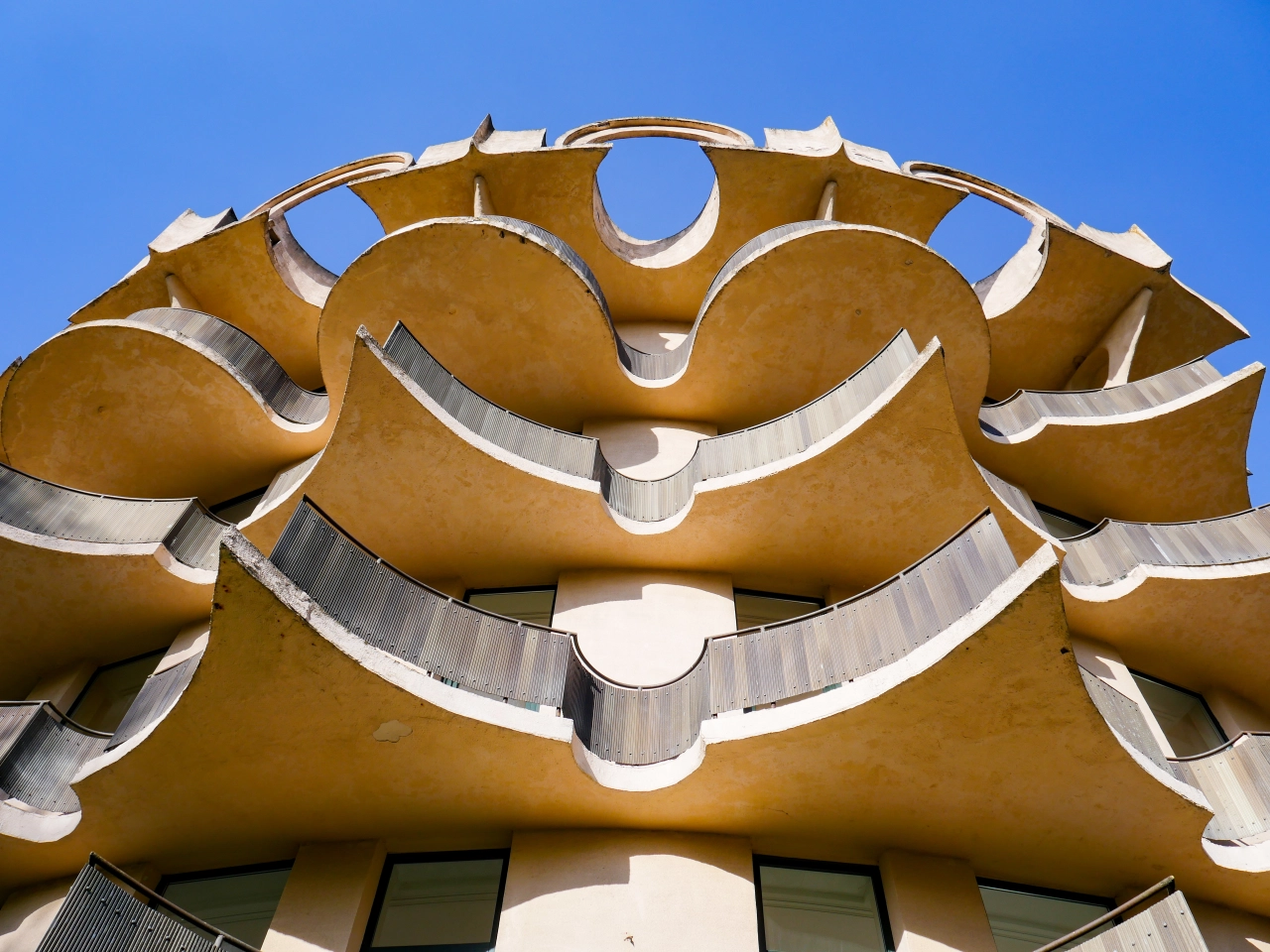Ornate golden concrete facade of Hotel Pusynas featuring symmetrical curved sculptural elements with white-painted details against a blue sky