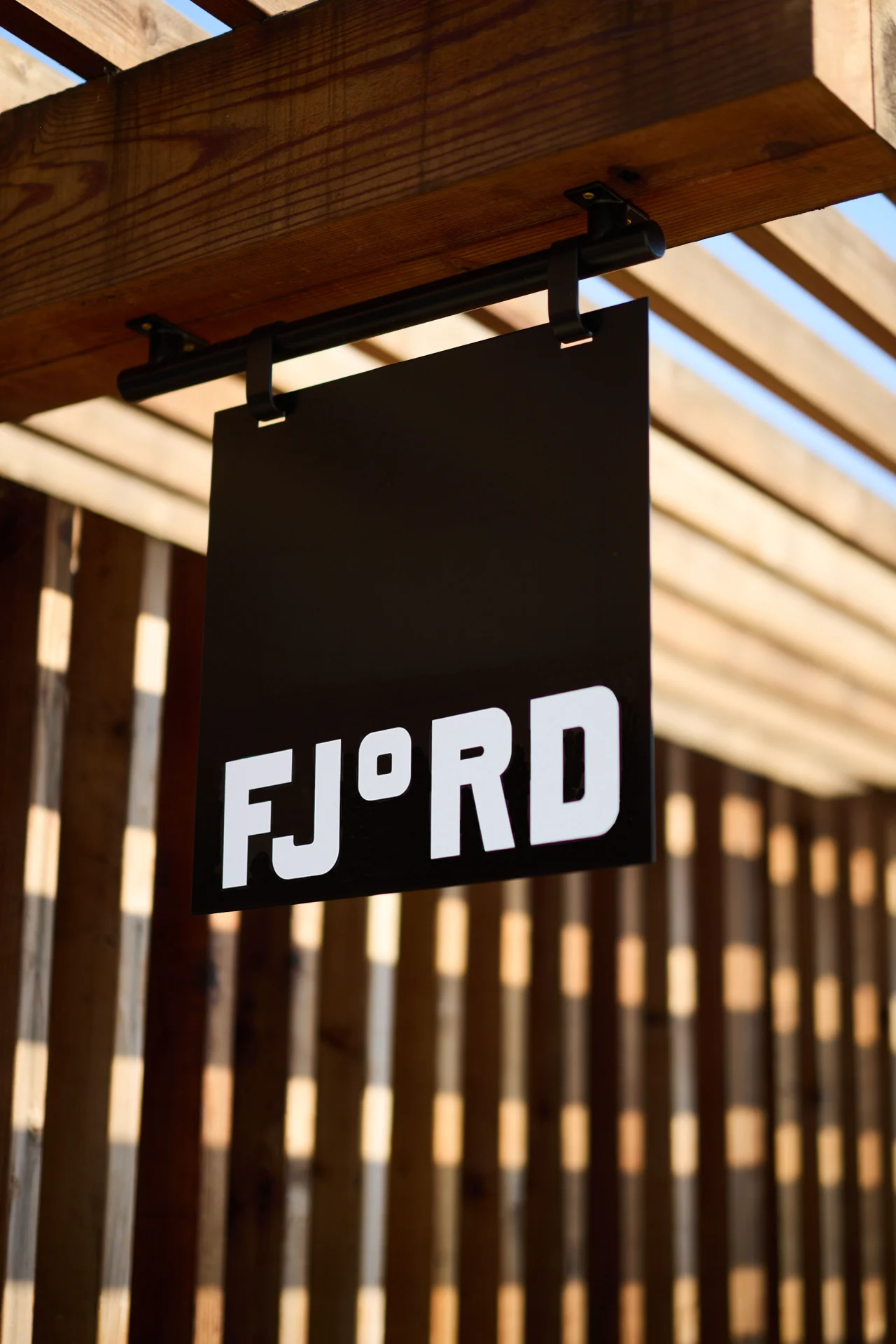 Black Fjord signage hanging from a wooden beam with slatted ceiling and natural light behind it
