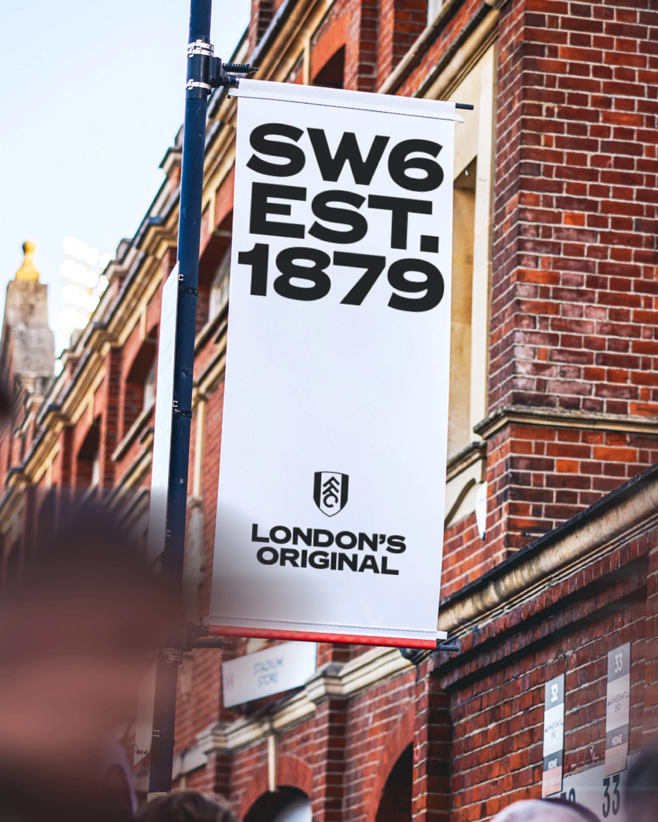 White banner hanging on red brick building reading SW6 EST. 1879 with London's Original logo below