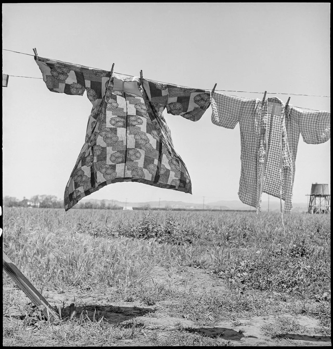 Laundry hanging on a clothesline in a desert landscape at Manzanar internment camp, with a barren field stretching behind it in black and white photography