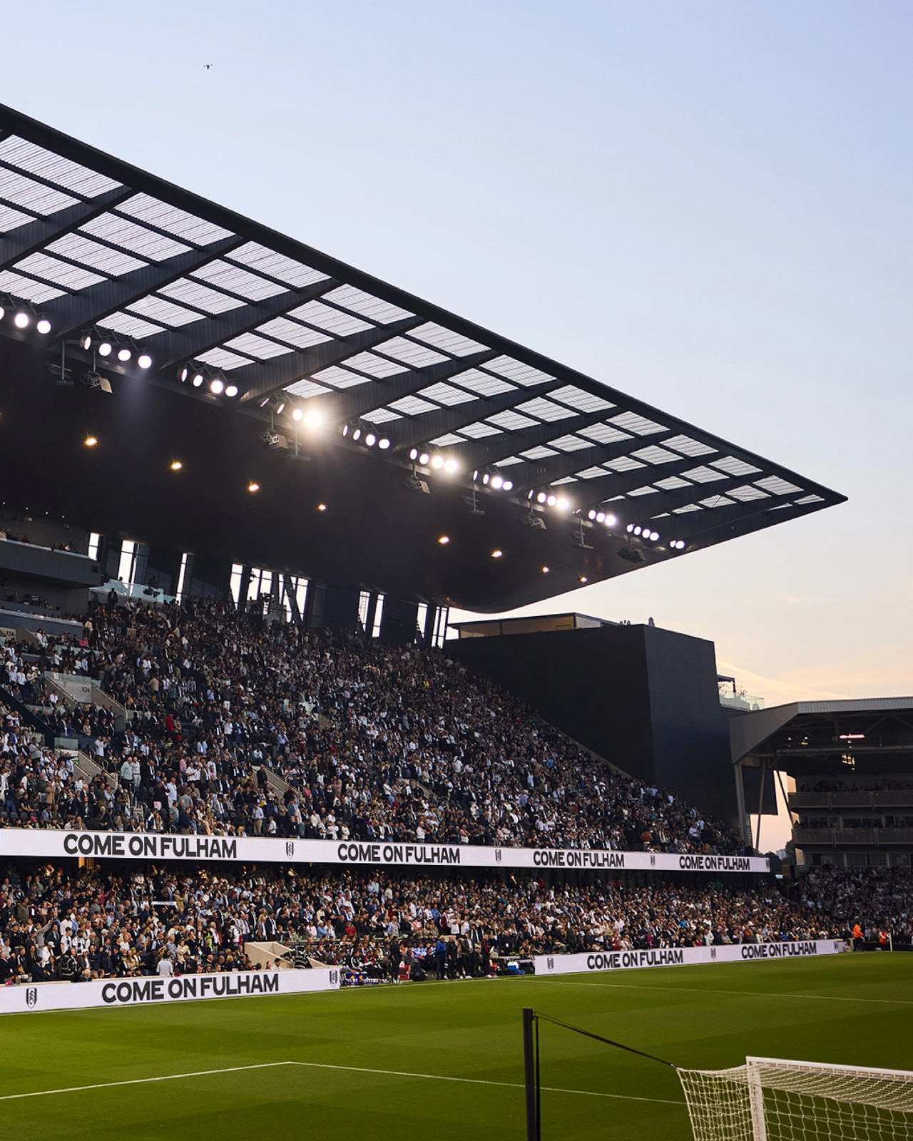 Fulham FC supporters filling the stands at Craven Cottage stadium with "Come On Fulham" advertising boards visible along the pitch perimeter