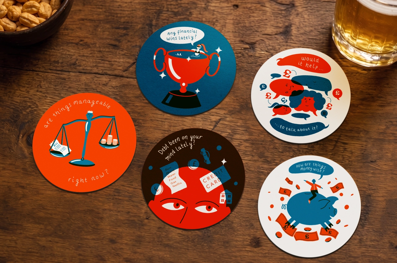 Five circular coasters arranged on a wooden surface featuring illustrated red and blue characters with text about debt and financial issues, part of the Say It Over a Drink campaign