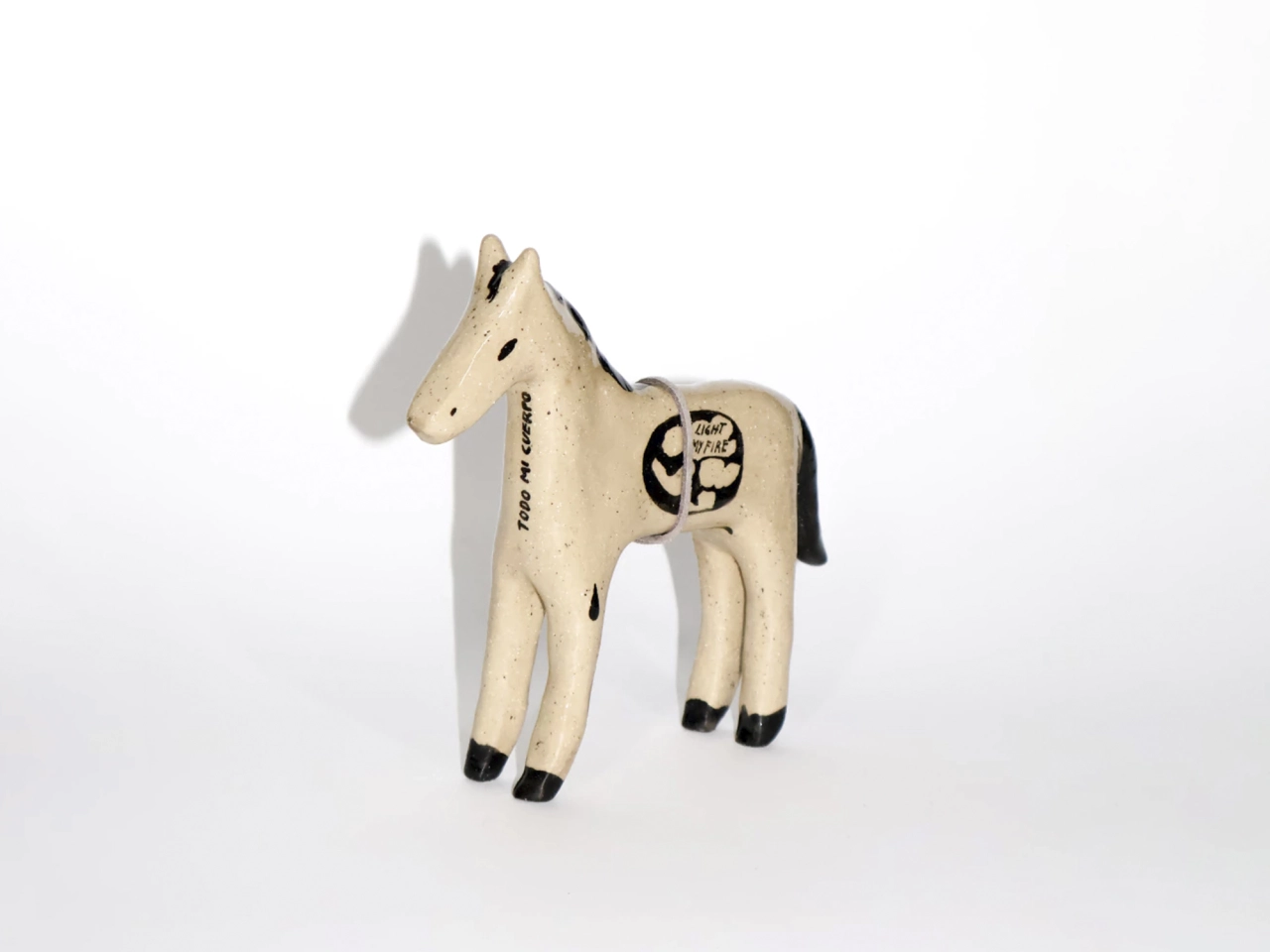 Cream-coloured wooden horse figurine with black hooves and decorative details on its side, casting a shadow on a white background