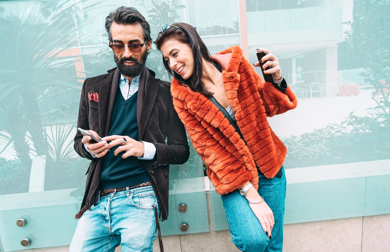 Two people examine a smartphone together against a turquoise glass backdrop in an urban setting