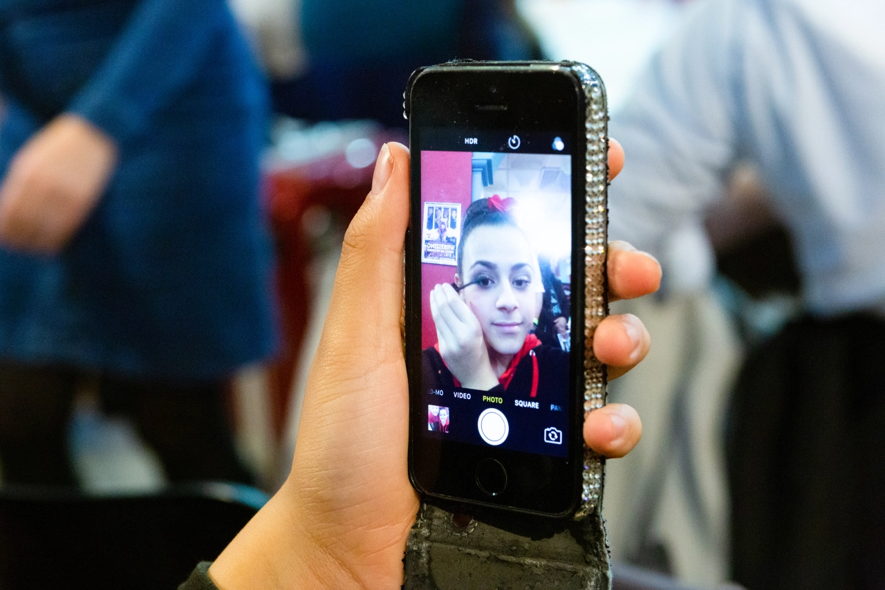 Hand holding a smartphone with camera app open, displaying a selfie of a young woman with roller skates visible in the blurred background