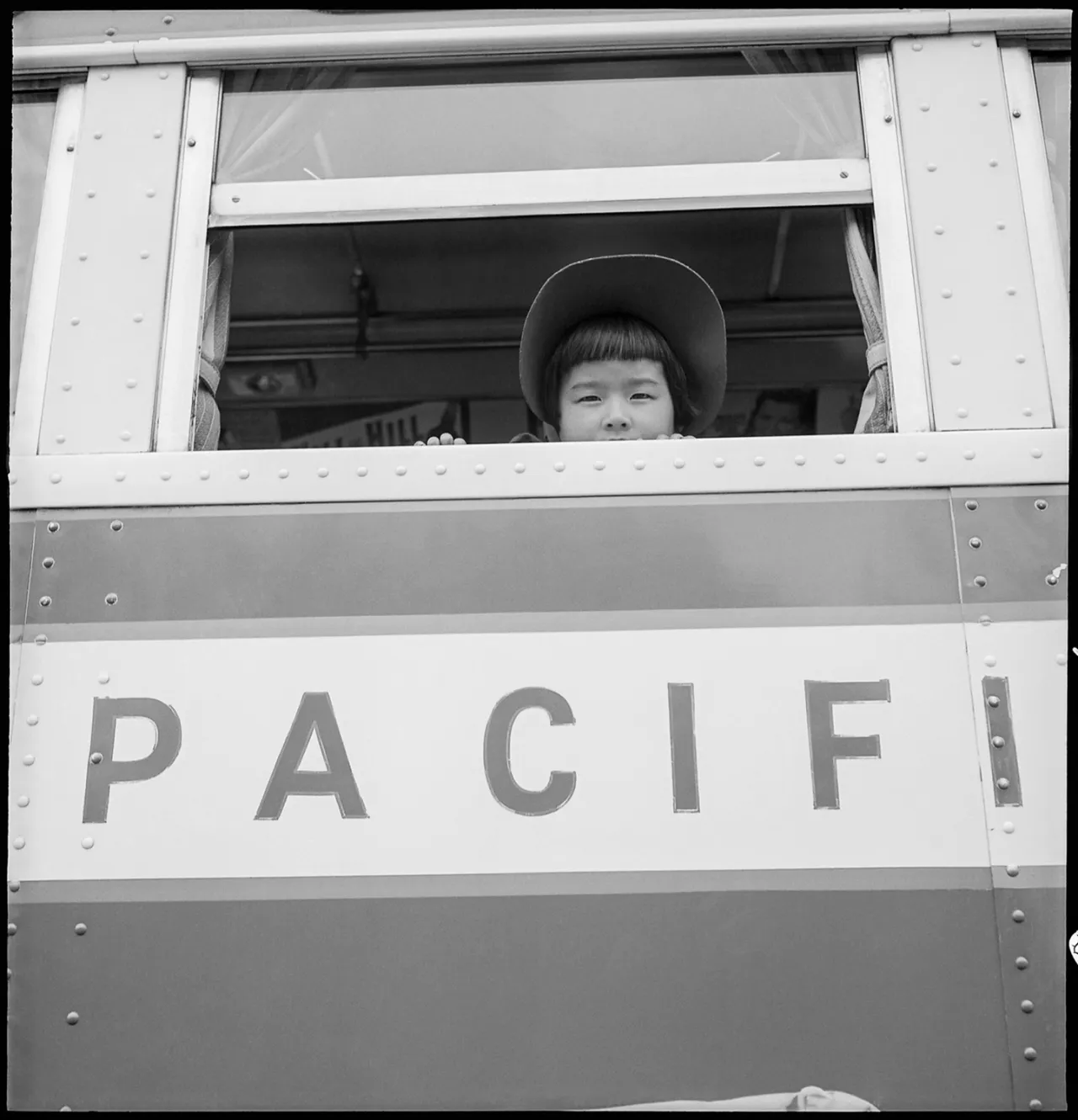Young child looking out the window of a Southern Pacific railroad car during Japanese American evacuation to Manzanar internment camp, 1942