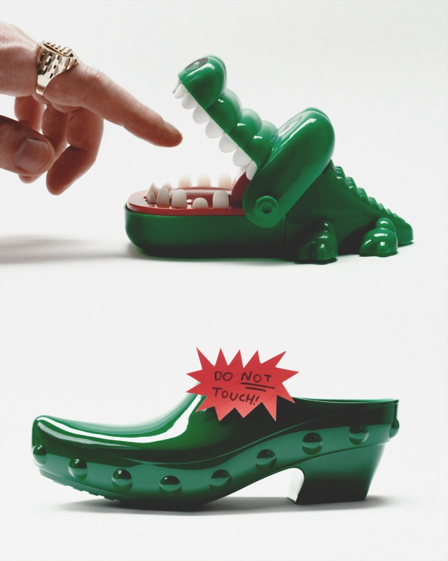 Hand with ring about to touch green crocodile toy with open mouth containing white teeth, with "Do Not Touch" warning label below