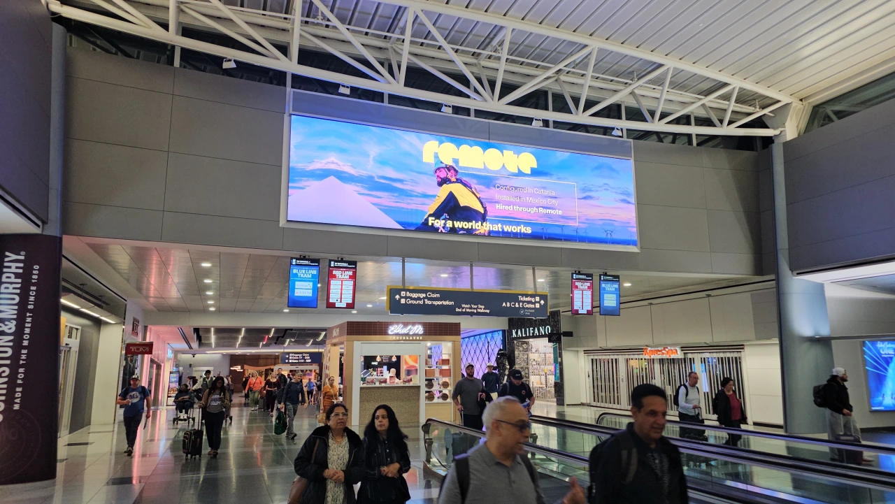 Remote's new branding displayed on a large screen above the concourse in a modern transport hub, with commuters walking below