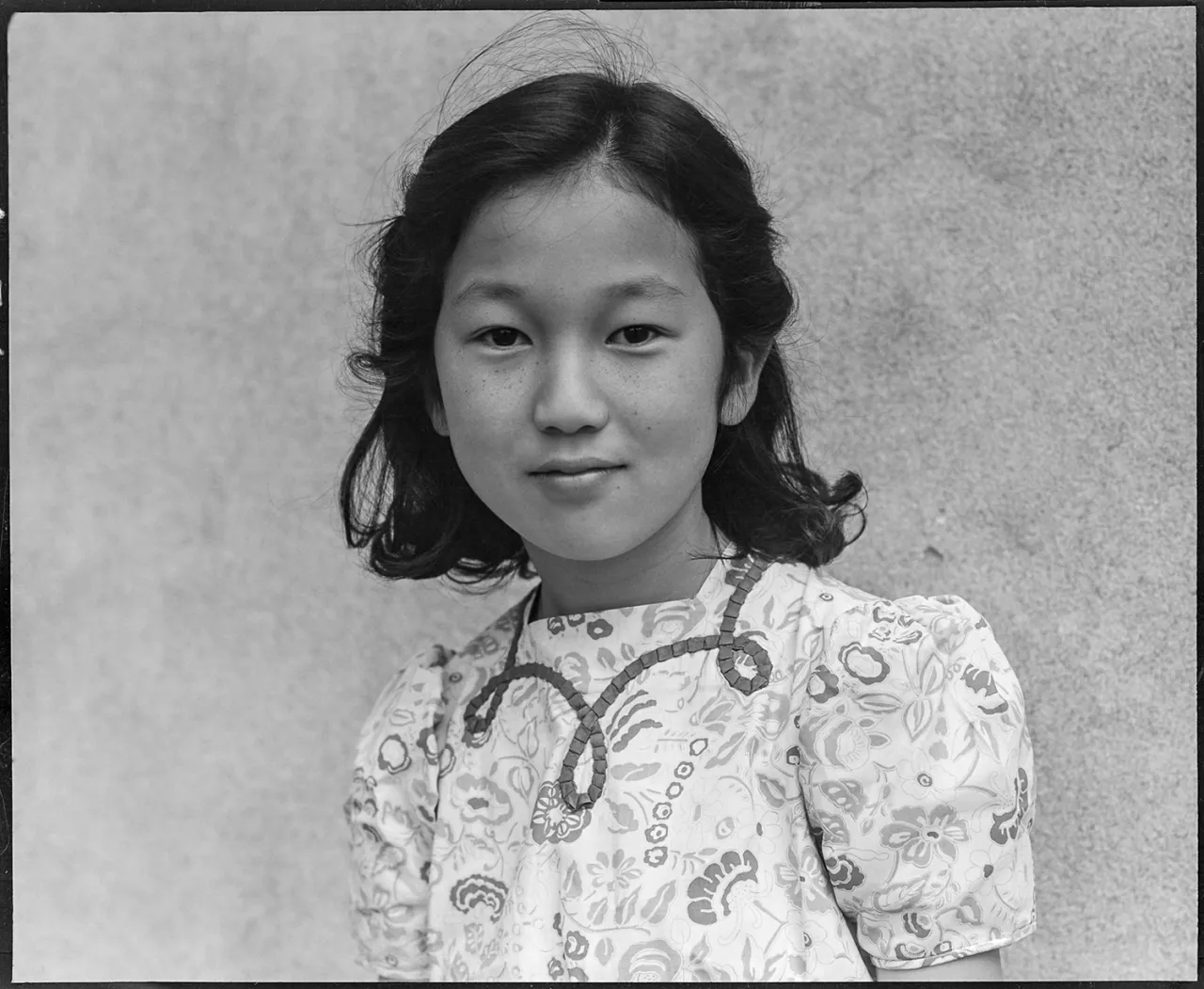 Black and white portrait photograph of a young Japanese American girl wearing a patterned short-sleeved shirt at Manzanar internment camp in the 1940s