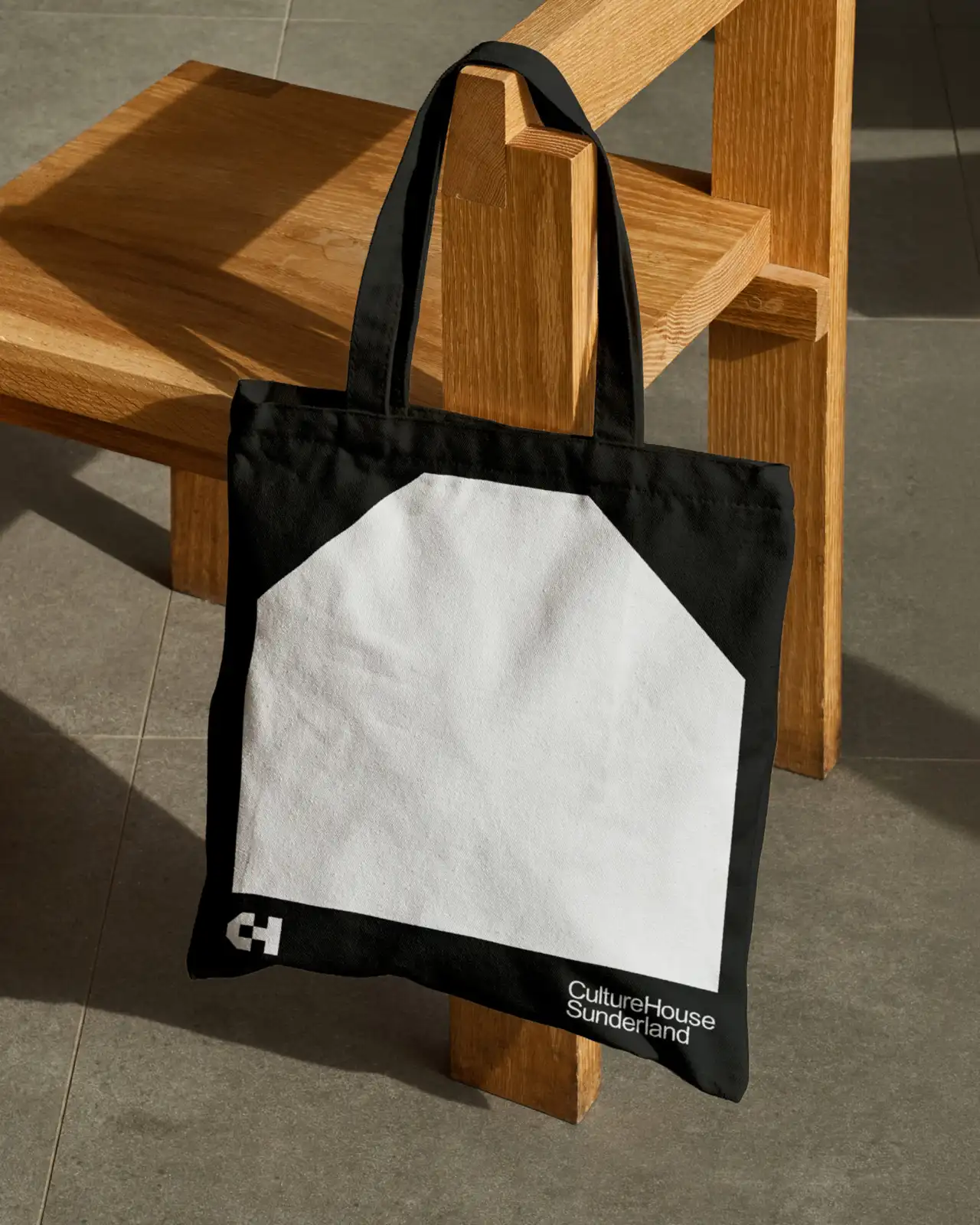 Black and white tote bag with Culture House Sunderland branding hung on wooden furniture in sunlit interior
