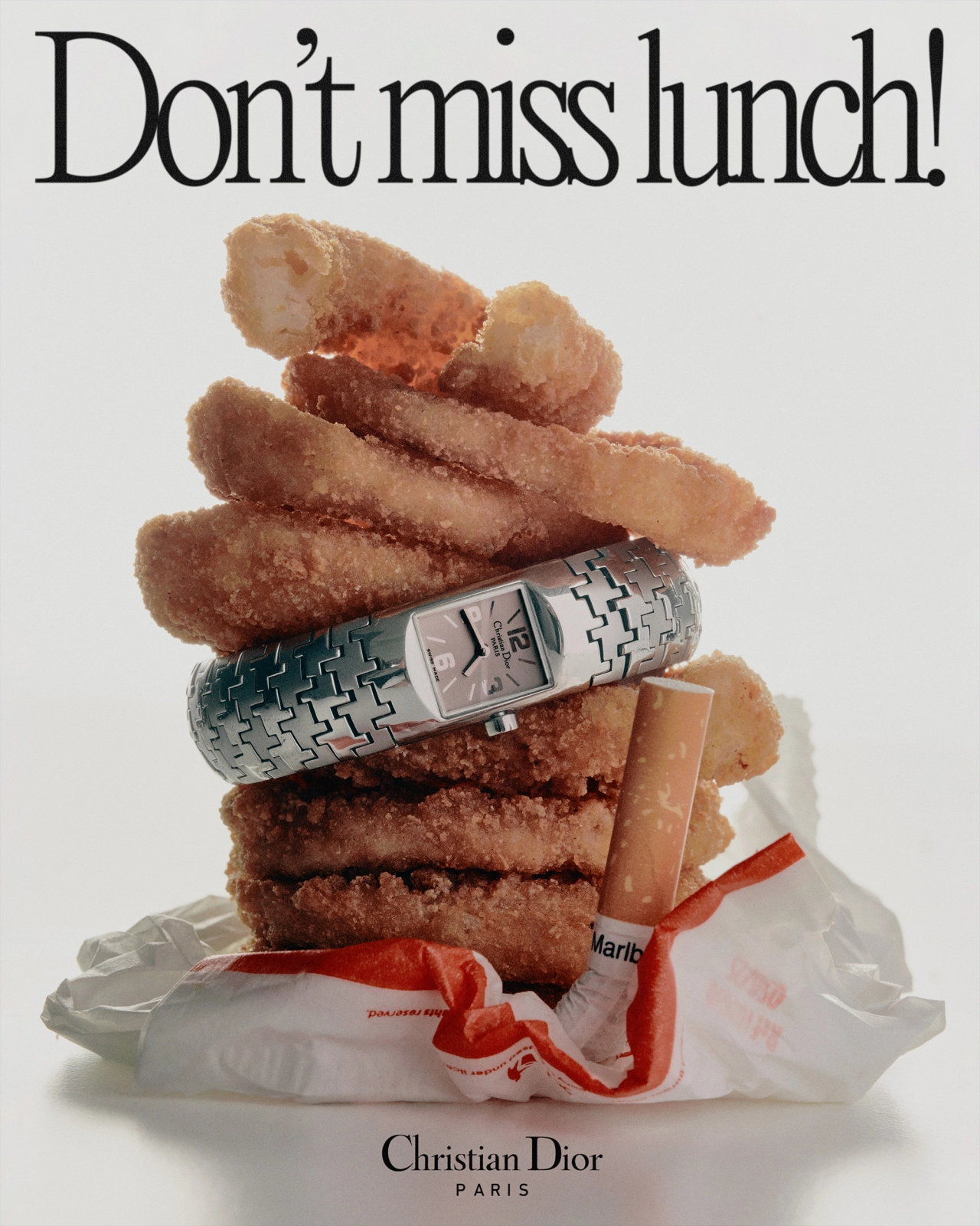 Stack of golden fried onion rings with a Christian Dior watch wrapped around the middle, next to a lipstick, on white packaging with "Don't miss lunch!" text above