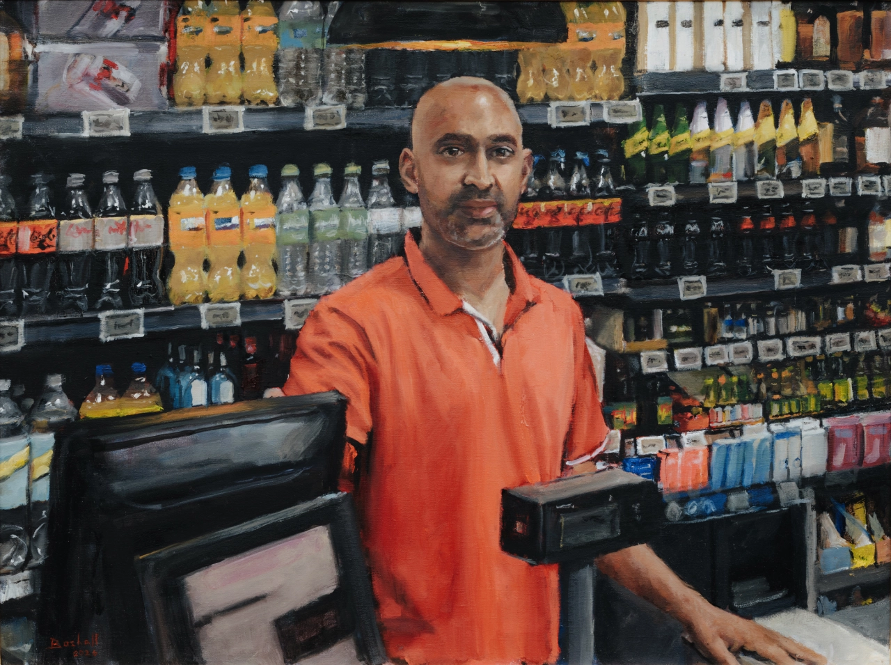 Man in orange shirt standing behind counter in a convenience shop stocked with drinks and snacks