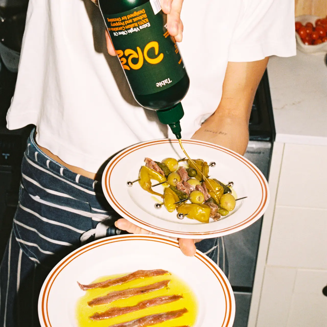 Person pouring Drzzl olive oil onto a plate of sautéed vegetables and another plate with drizzled yellow oil