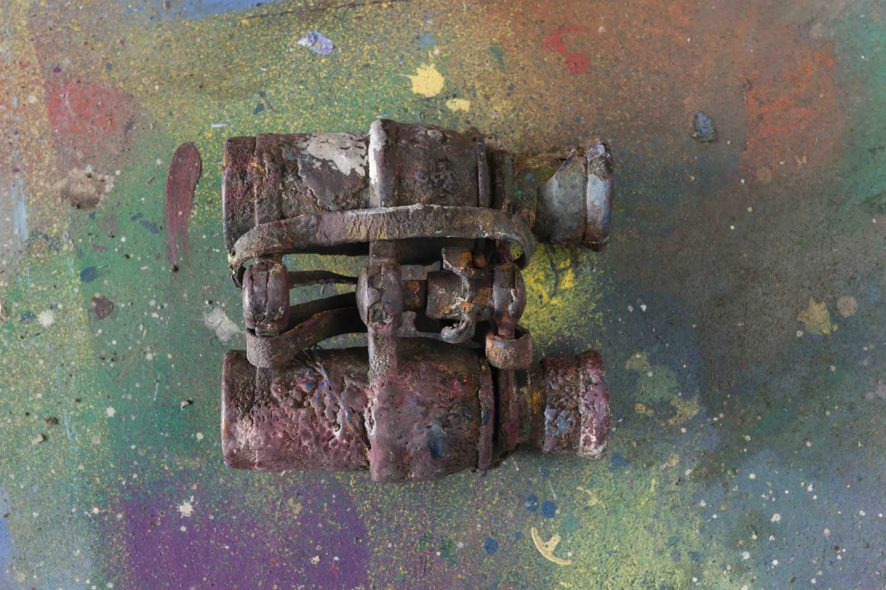 Weathered metal clamp or vise with rusted surfaces, photographed against a colourful paint-splattered ground, possibly from Sidney Nolan's studio