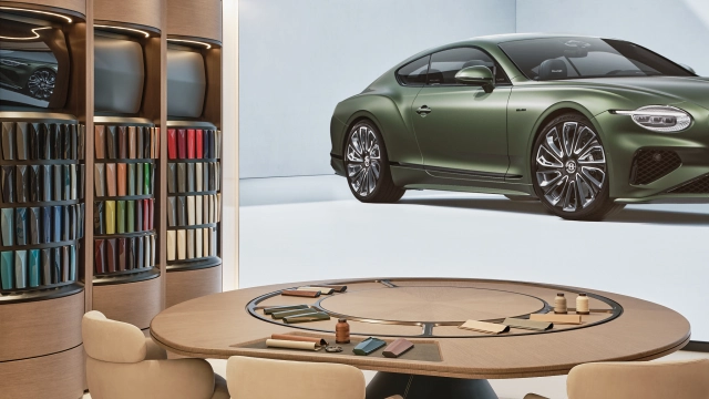 Green Bentley sports car displayed on a screen above a round wooden table with a fabric swatch carousel and cream seating in the showroom lounge area