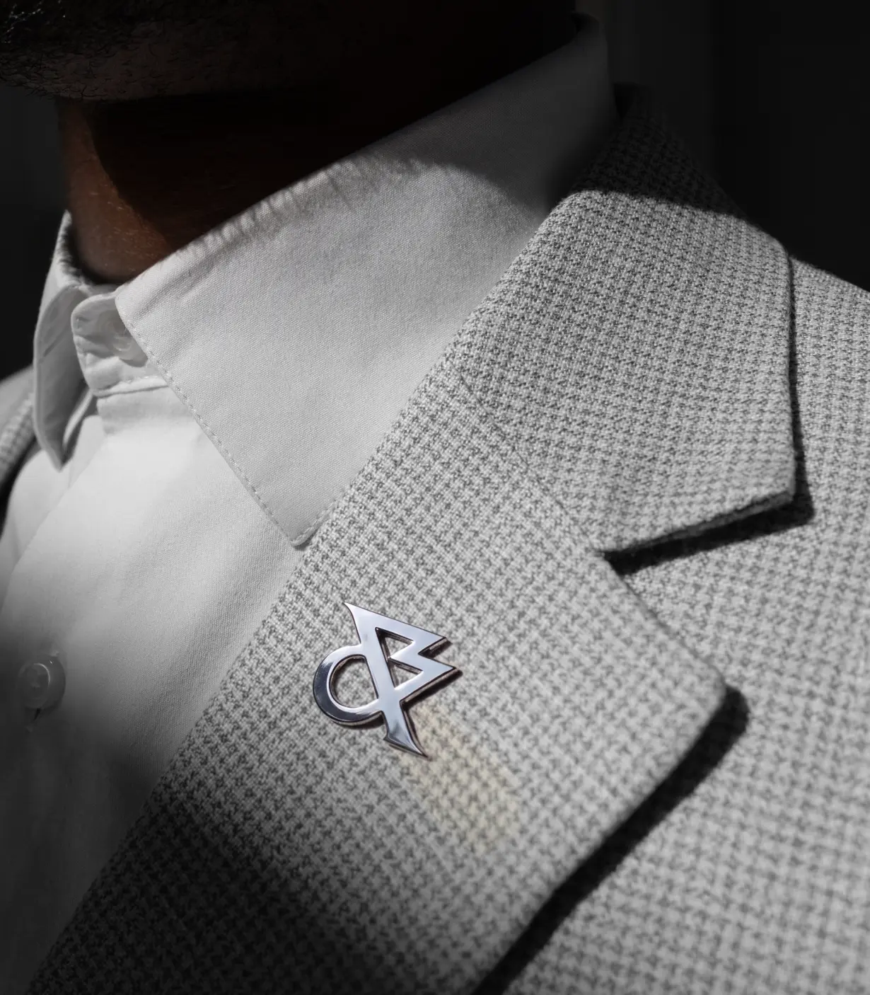 Close-up of a textured grey jacket lapel with White & Case's new angular logo badge in metallic silver, worn with a white shirt