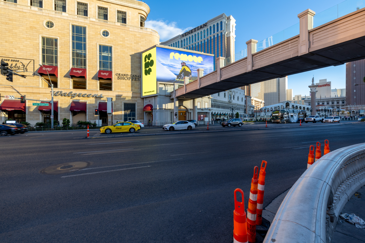 Urban street scene showing a yellow taxi, white car and red traffic cones on a Las Vegas boulevard with vintage yellow building and overhead bridge
