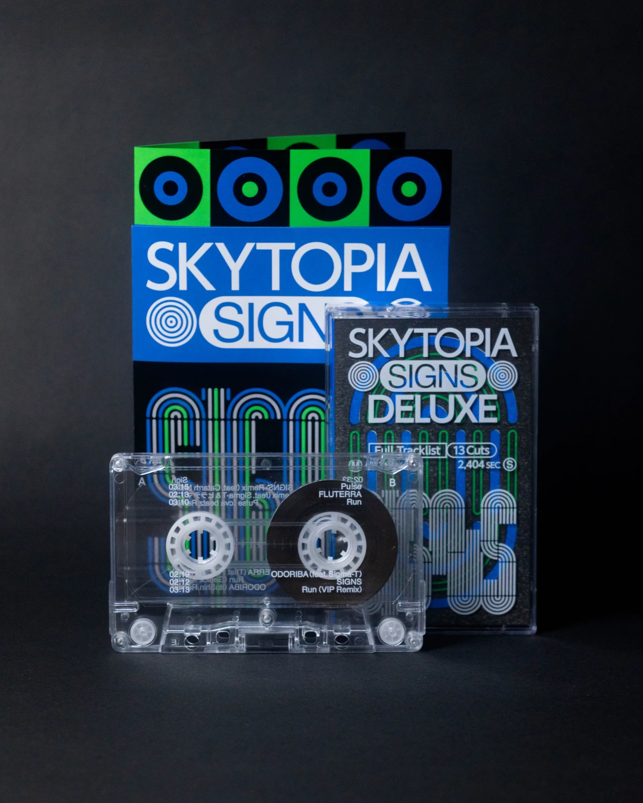Skytopia Signs Deluxe cassette tape and DVD case displayed alongside a clear cassette tape against a dark background