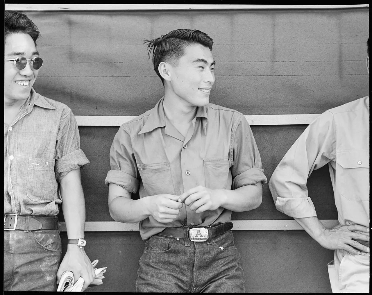 Three young men in work shirts leaning against a wooden structure at Manzanar internment camp