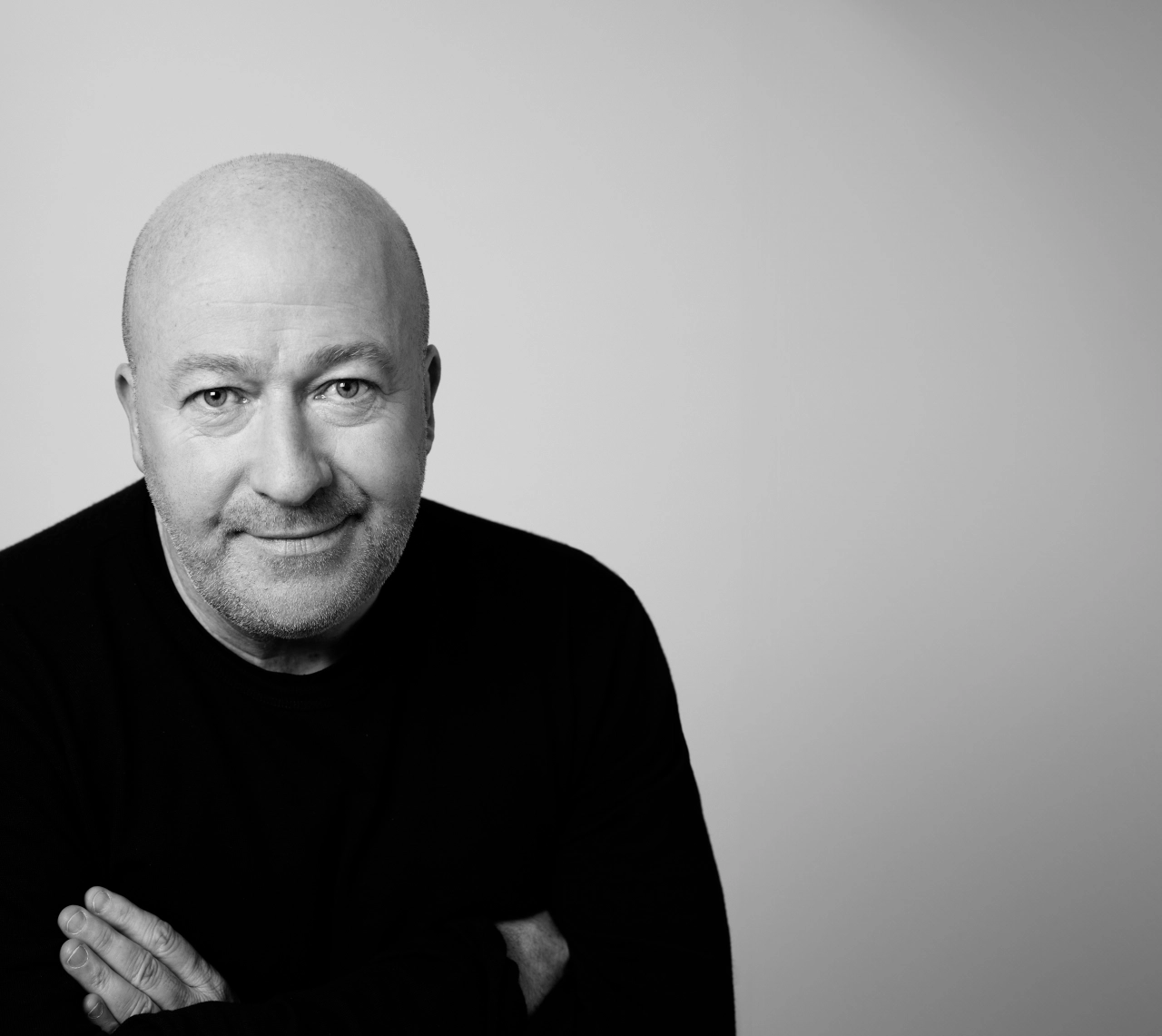 Black and white portrait photograph of Bryan Edmondson, founder of SEA design studio, wearing a black jumper with arms crossed against a plain background