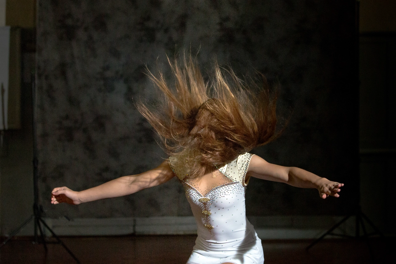 Young roller skater in white dress with arms outstretched and hair in motion, photographed in a domestic interior setting